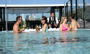 2 couples taking a dip in the pool while drinking with a waiter serving them