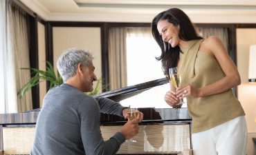 Man and woman leaning on a piano holding wine glass