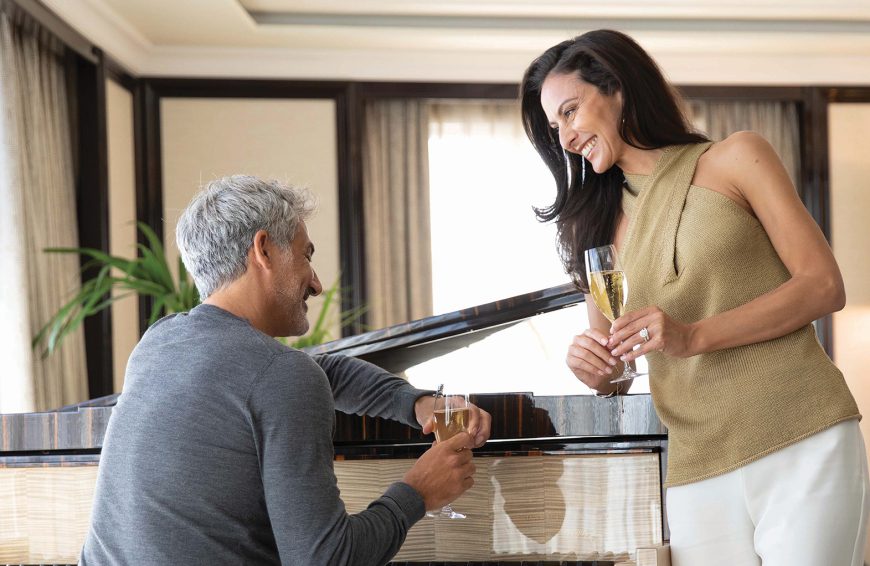 Man and woman leaning on a piano holding wine glass