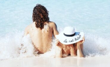 a woman and a man on a beach nude with a hat that says Do Not Disturb on it