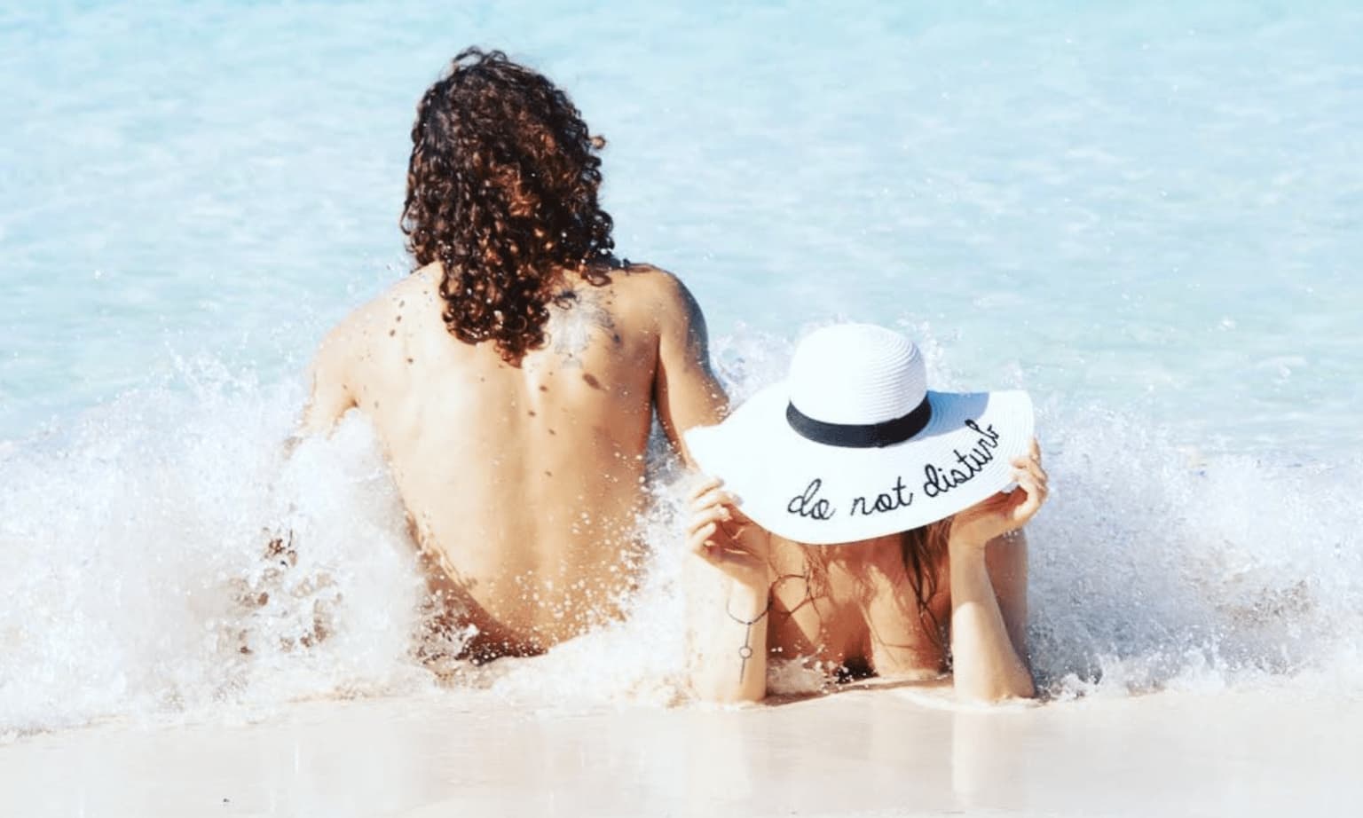 a woman and a man on a beach nude with a hat that says Do Not Disturb on it