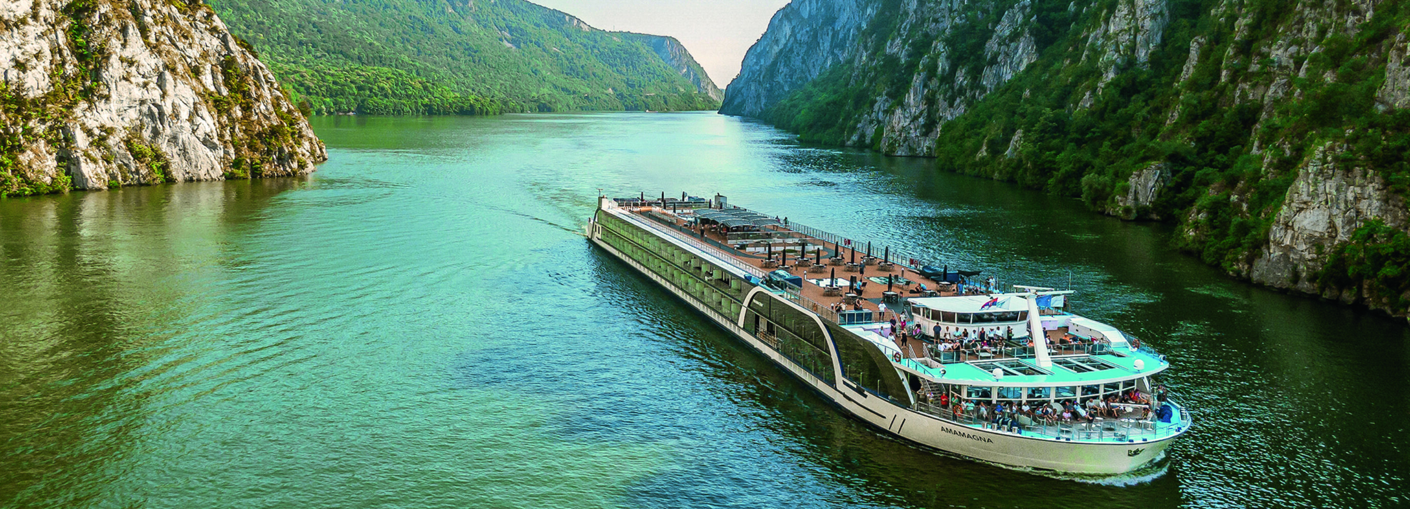 An exterior view of AmaMagna sailing through a gorge. It is twice the width of almost every other river ship in Europe.