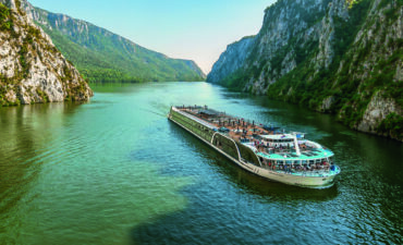 An exterior view of AmaMagna sailing through a gorge. It is twice the width of almost every other river ship in Europe.