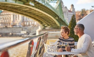 Uniworld couple sititng on a ship under a bridge in Europe