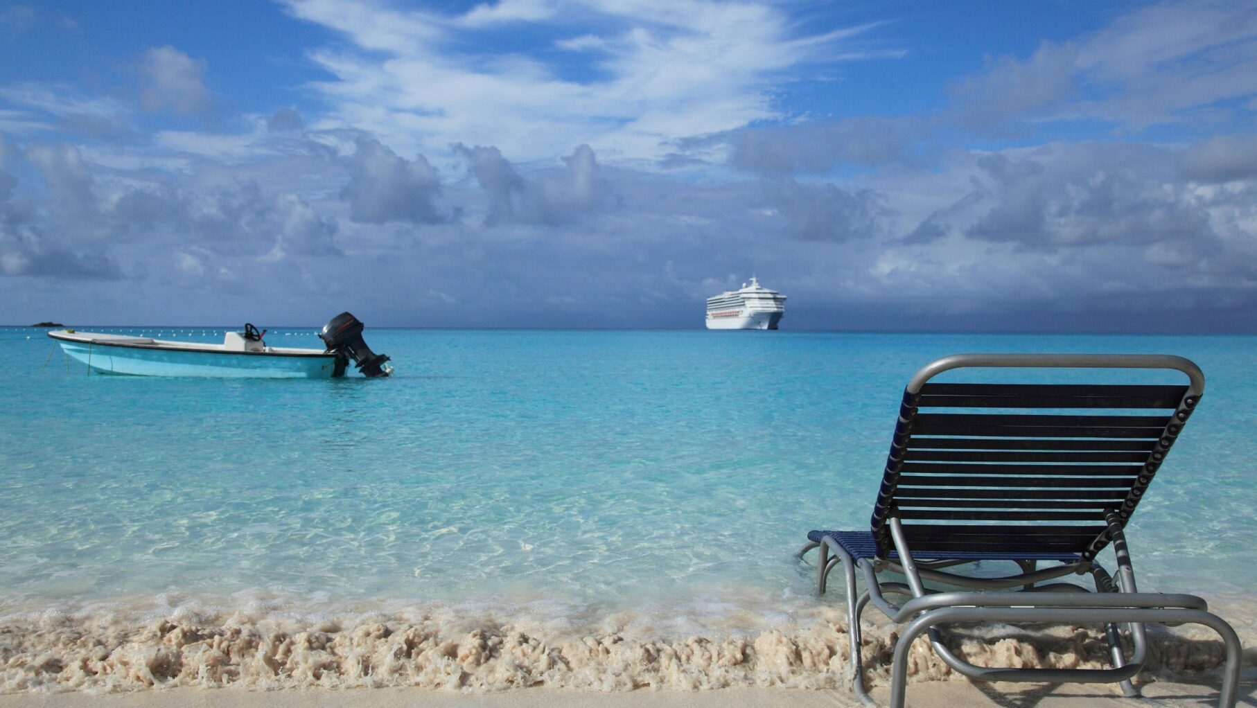 A cruise ship sails in the distance from a bright beach.