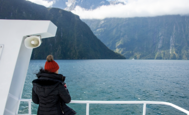 Woman looks off boat over Milford Sound landscape.