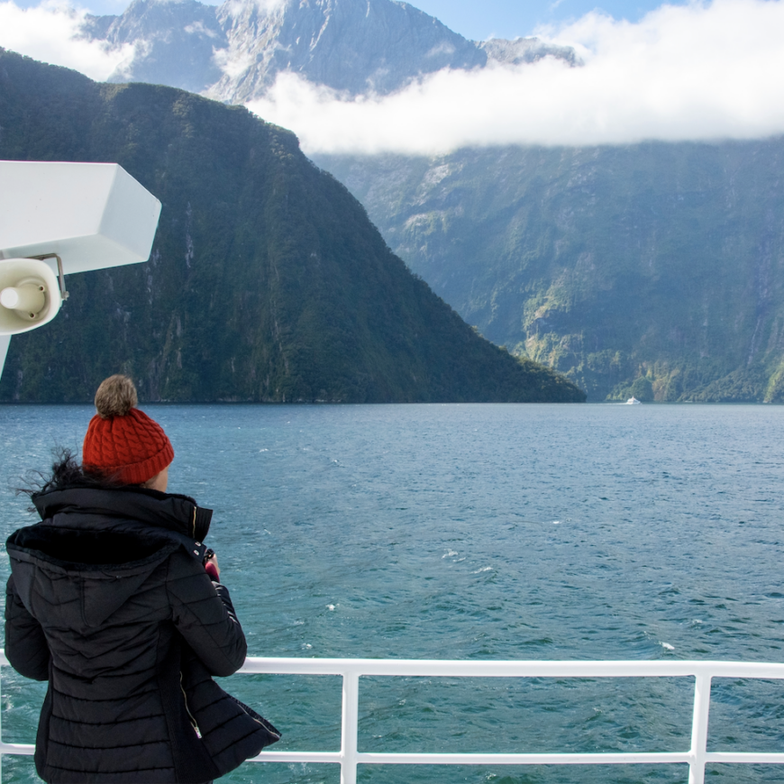 Woman looks off boat over Milford Sound landscape.