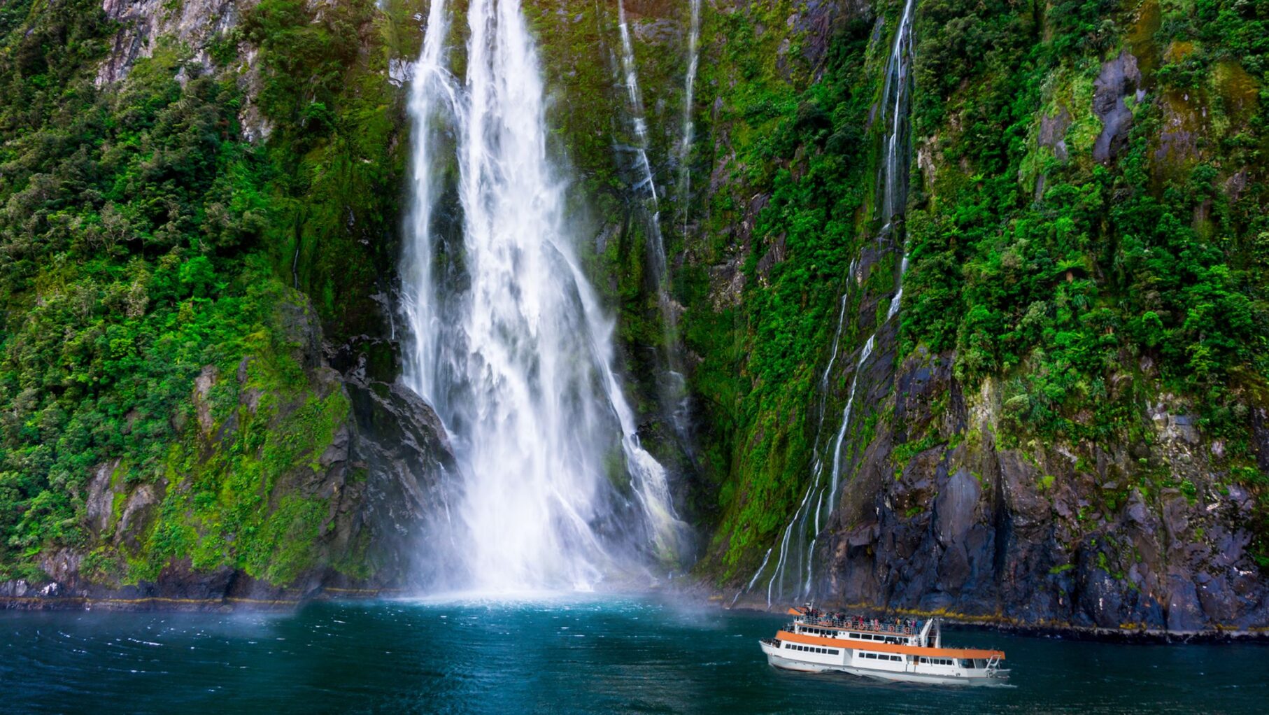 A small ships sails up to a waterfall in Milford Sound.