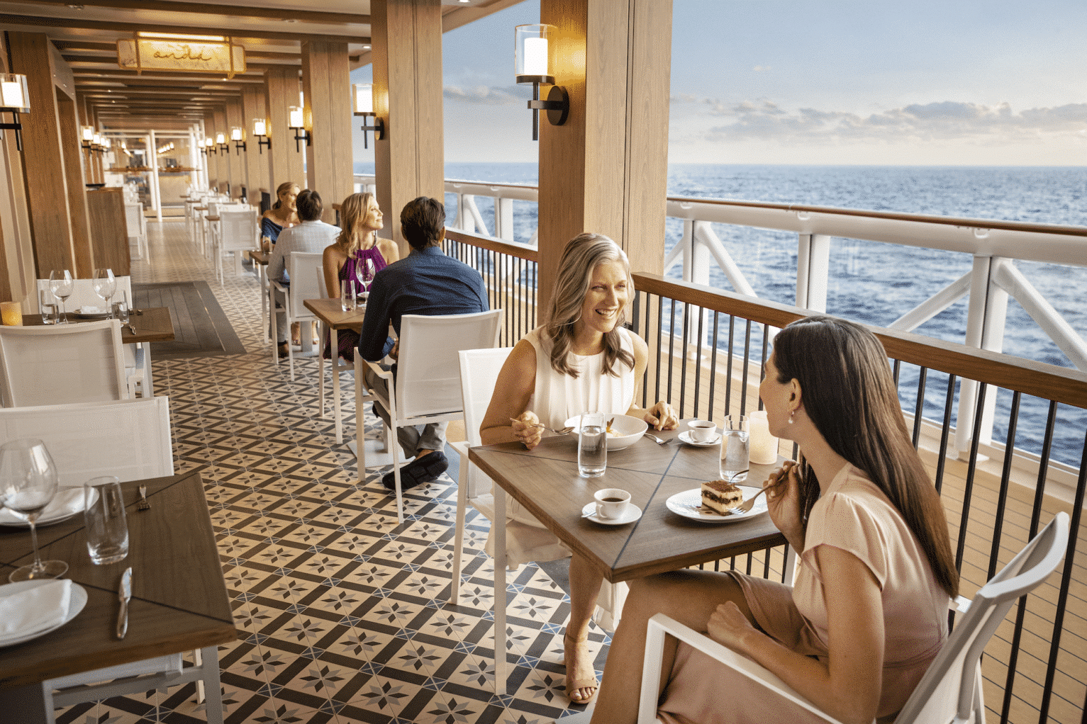 Two women dine on a ship's deck with the ocean in the background