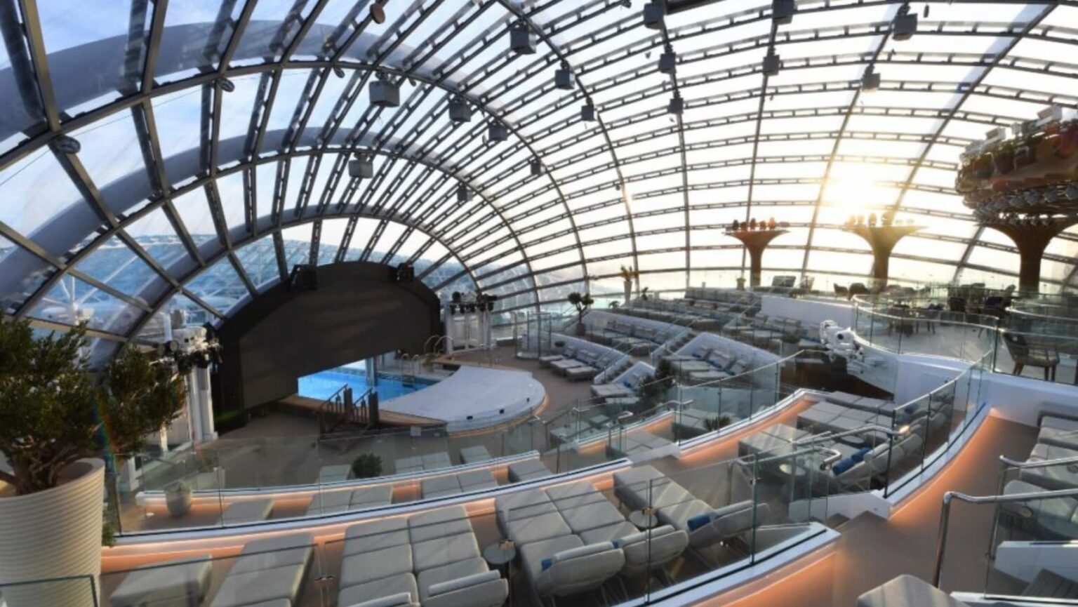 Glass-domed lounge with white seating around a pool and stage