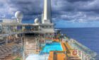Cruise ship pool deck with chairs under a partly cloudy sky, ocean view