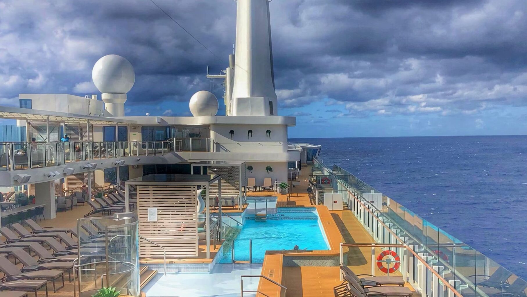 Cruise ship pool deck with chairs under a partly cloudy sky, ocean view