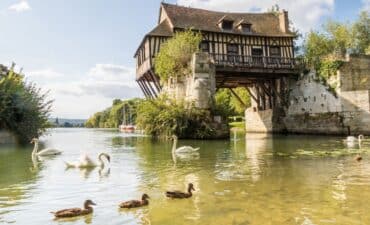 Swans and ducks swimming in front of the beautiful old mill on the broken bridge over Seine river in Vernon, Normandy, France