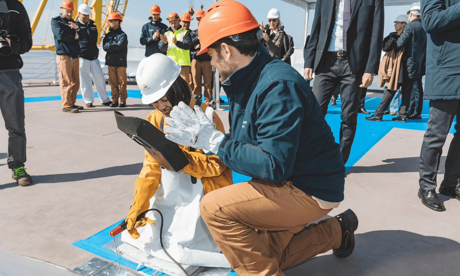 Two people crouch down to weld ceremonial coins onto the mast of Viking Libra