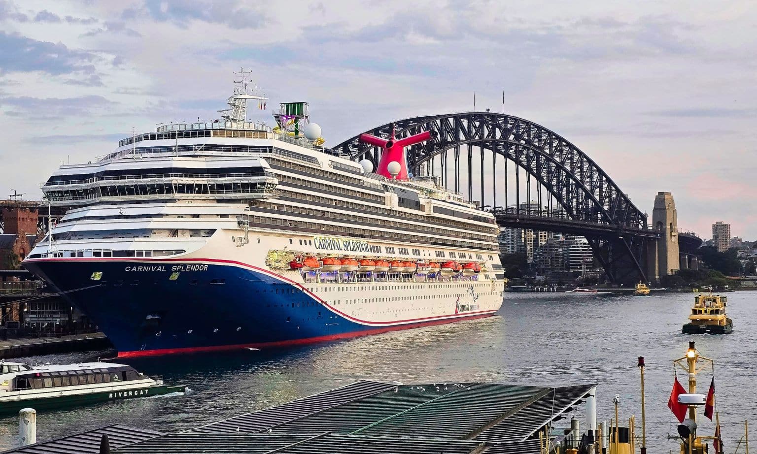 A large cruise ship docks in Sydney with Sydney Harbour Bridge in the background.