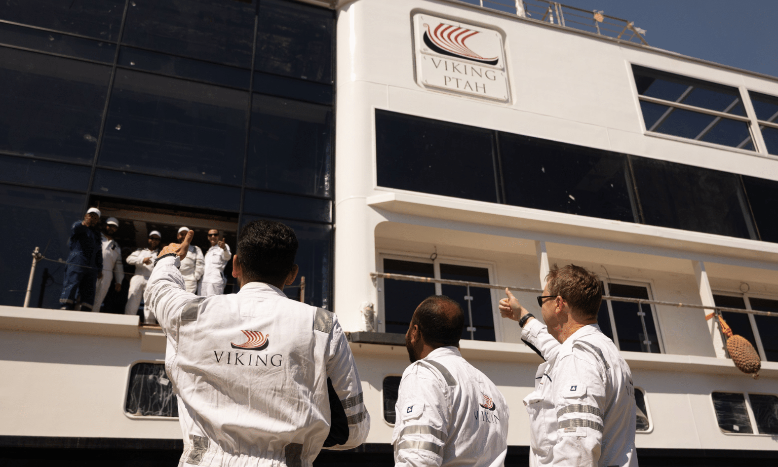 Three men raise thumbs up to river cruise ship Viking Ptah