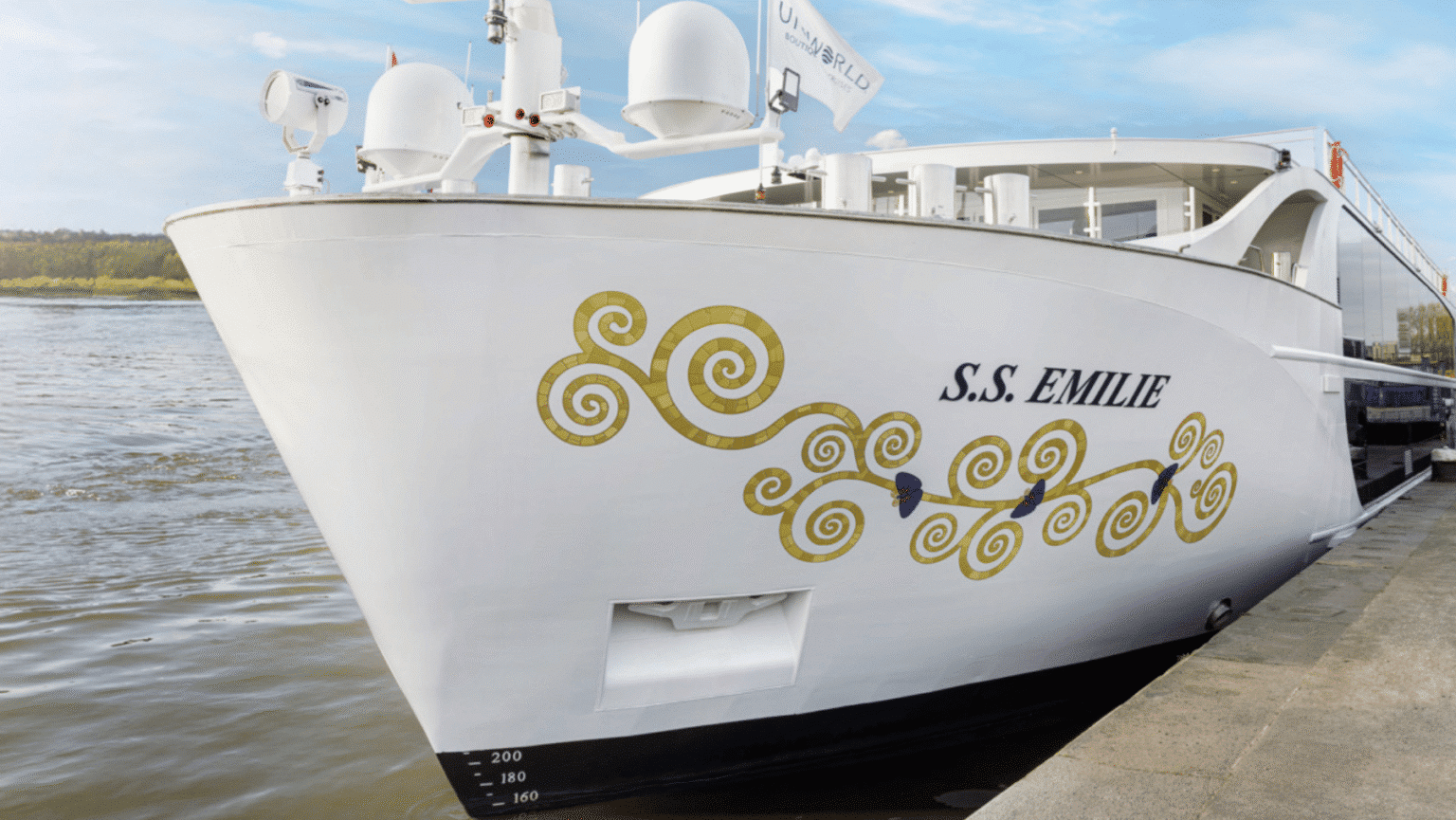 A white cruise ship with gold swirls on the hull on water