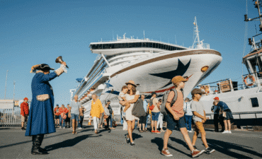 a town crier rings a bell as passengers from a cruise ship walk by