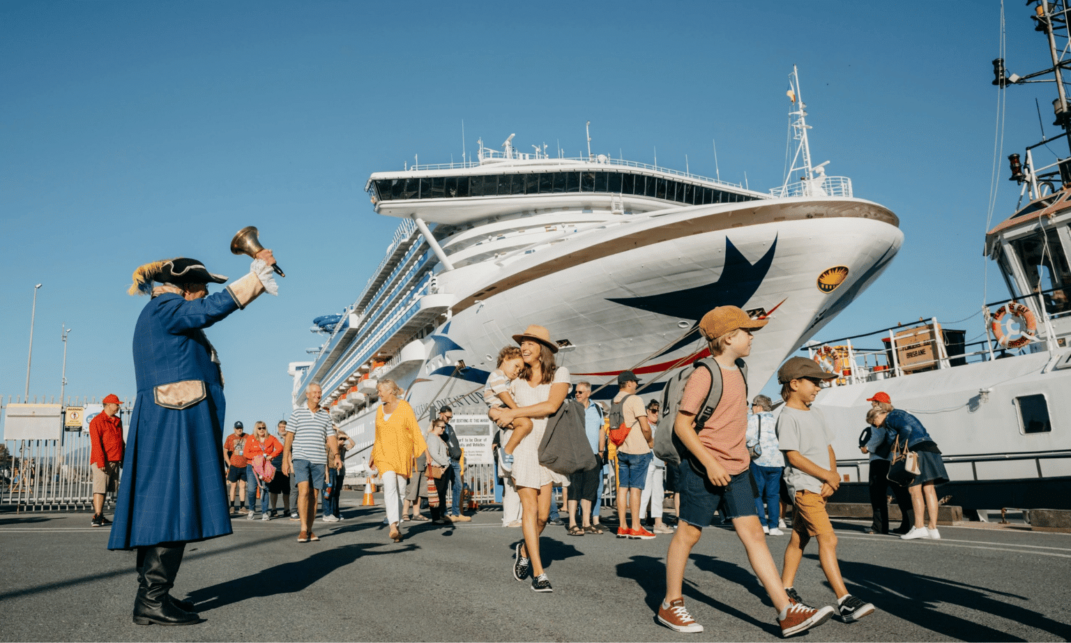 a town crier rings a bell as passengers from a cruise ship walk by