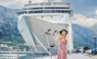 A young woman in a pink dress stands in front of a large cruise ship