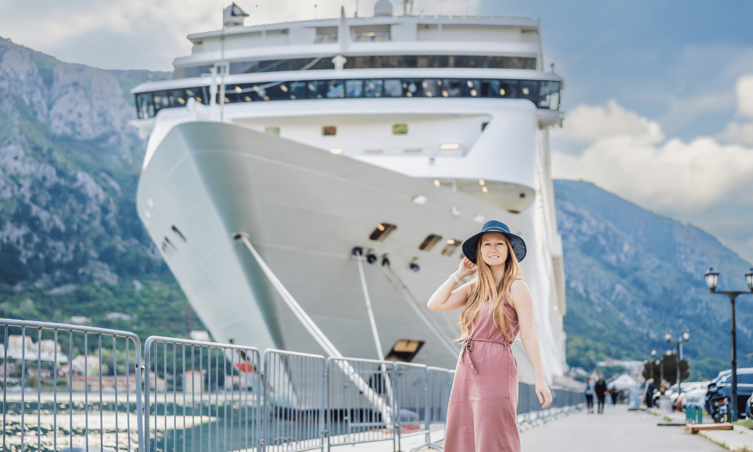 A young woman in a pink dress stands in front of a large cruise ship