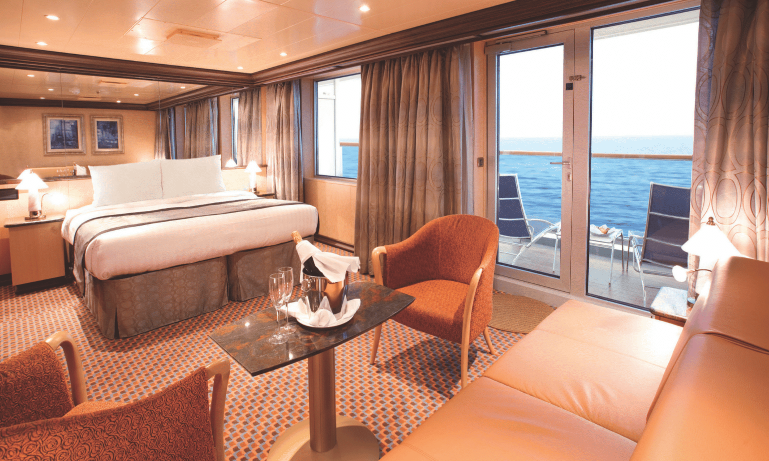 a cabin on a cruise ship with a bed, small table, chairs and a bottle of champagne on the table