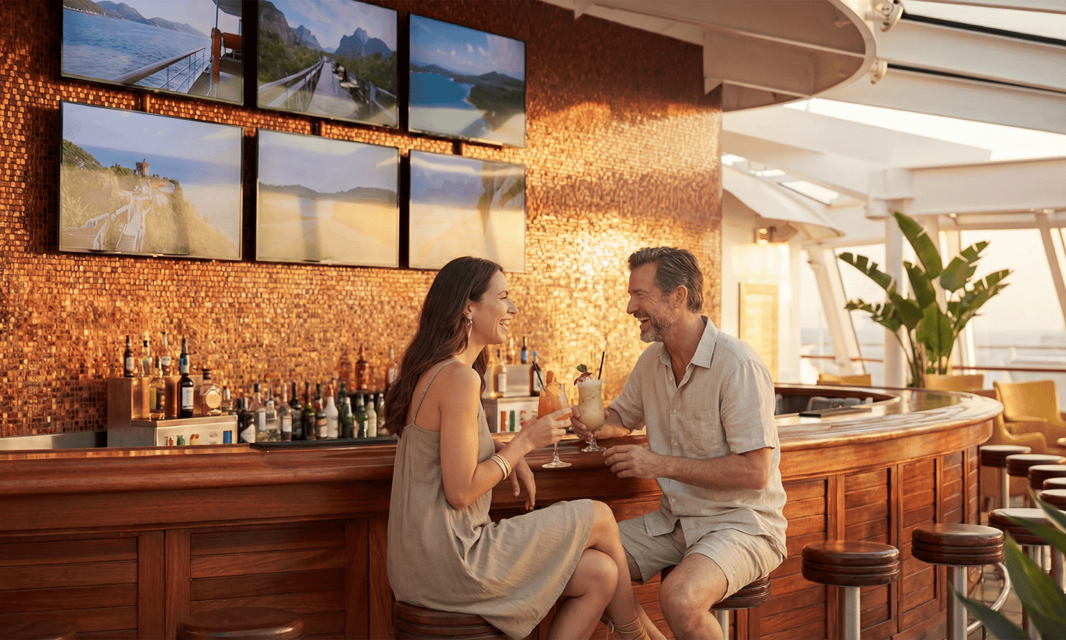 A woman and a man sit in relaxed beige clothing sit at a bar on a cruise ship