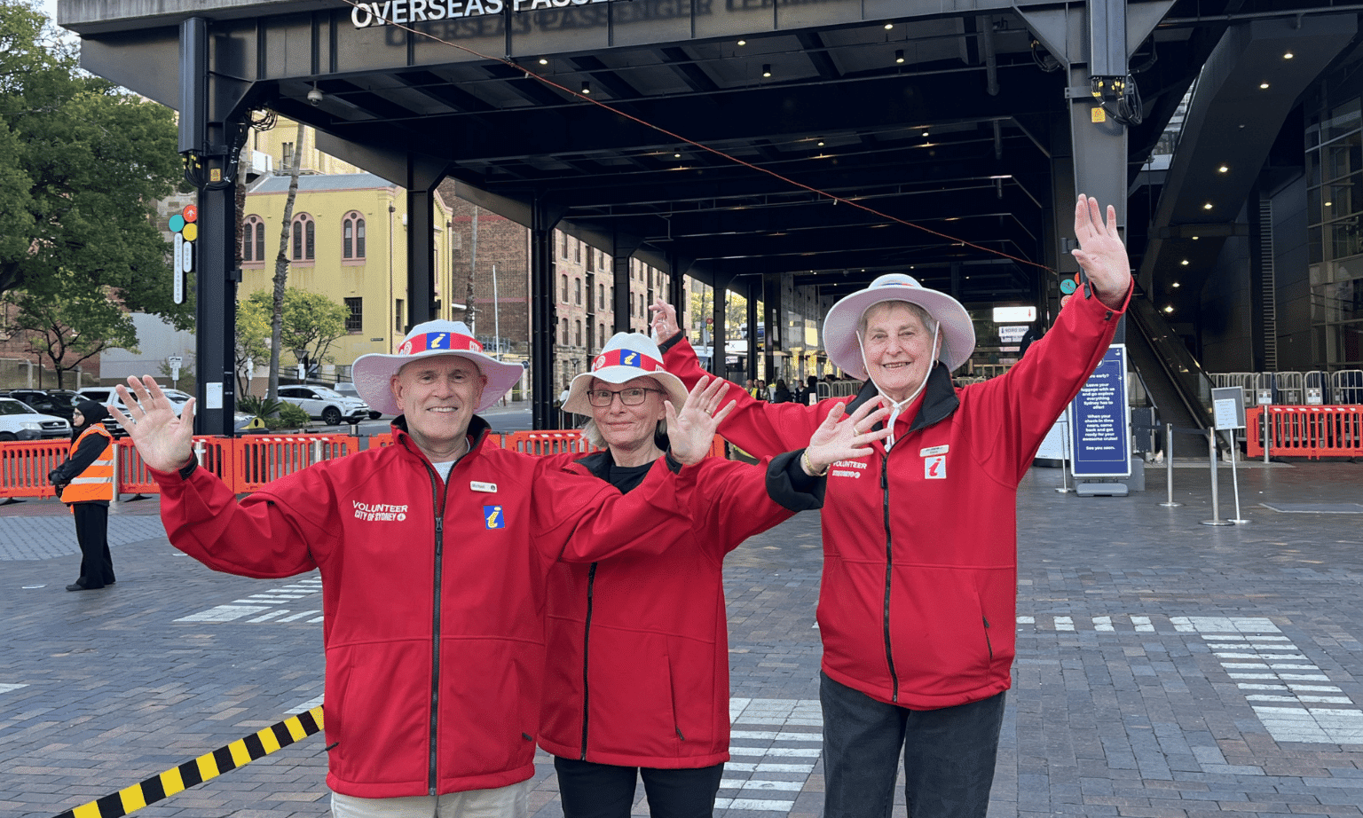 Three people in red jacket with their hands in the air looking happy